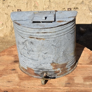 Pode incluir: Um refrigerador de água vintage de metal galvanizado com uma tampa articulada e uma torneira de latão. O refrigerador está desgastado e mostra sinais de ferrugem.