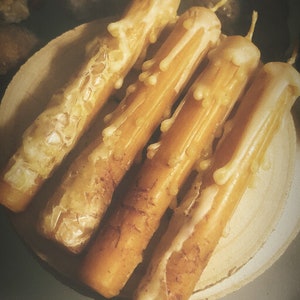 Può includere: Quattro candele di cera d'api gialle con una superficie testurizzata e gocciolante. Le candele sono disposte su una superficie di legno.