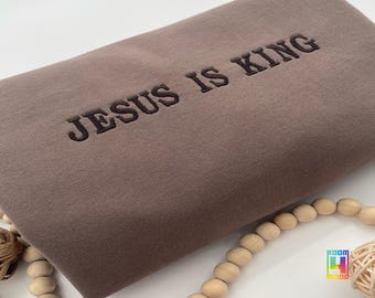 May include: A brown sweatshirt with the text "JESUS IS KING" embroidered in black.