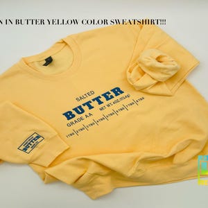 May include: A yellow sweatshirt with the text "SALTED BUTTER GRADE AA NET WT. 402. (113.4g) 178g | 278g | 378g | 478g | 578g | 778g | 878g" printed on the front.