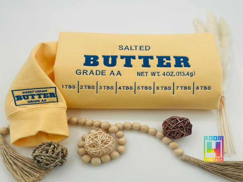 May include: Yellow sweatshirt with a graphic of a butter stick label. The label reads "Salted Butter Grade AA Net Wt. 4 oz. (113.4g)" and has a measurement guide in tablespoons.