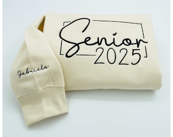 Può includere: Una felpa color crema con ricamo nero che dice "Senior 2025" in un riquadro. La parola "Senior" è in corsivo. Il nome "Gabriela" è ricamato sulla manica sinistra.