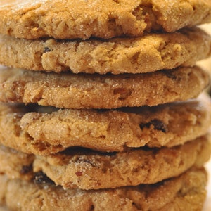 Puede incluir: Una pila de seis galletas de azúcar moreno con una ligera capa de azúcar en polvo en la parte superior. Las galletas están dispuestas sobre una superficie con un patrón blanco y rojo.