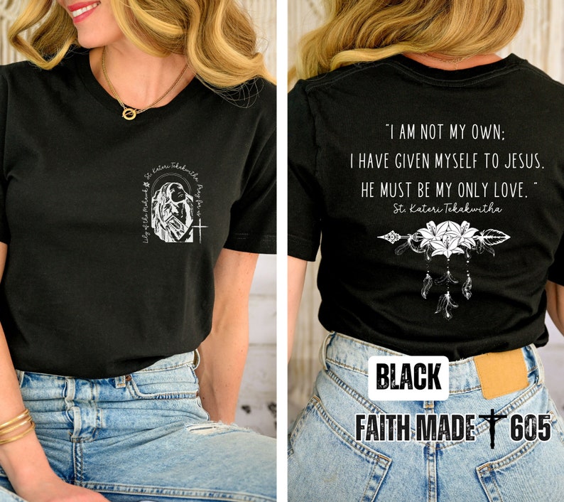 May include: Black t-shirt with a white graphic of a woman praying with the text "Lily of the Valley" and "St. Kateri Tekakwitha Pray for us". The back of the shirt has a white graphic of an arrow with flowers and the text "I am not my own: I have given myself to Jesus. He must be my only love. - St. Kateri Tekakwitha". The shirt also has the text "BLACK" and "FAITH MADE 605".