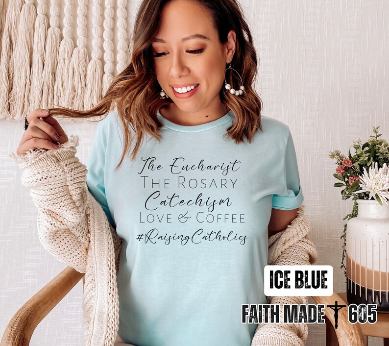 May include: Ice blue t-shirt with the text "The Eucharist, The Rosary, Catechism, Love & Coffee, #Raising Catholics." The shirt also has the text "ICE BLUE" and "FAITH MADE 605".