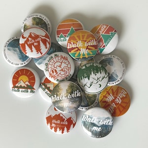 Puede incluir: Un conjunto de botones redondos con el texto "Walk with Me" y varios diseños temáticos de la naturaleza. Los botones presentan ilustraciones de montañas, bosques y puestas de sol en tonos naranja, verde y azul. Algunos botones incluyen el texto "Moses 6:34".