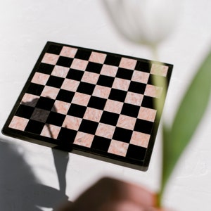 May include: A black and pink marble chessboard with a white flower and green stem in the background.
