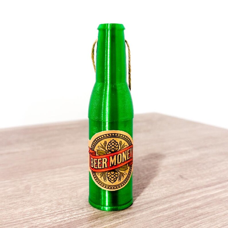 Puede incluir: Una botella de vidrio verde con una etiqueta que dice "Beer Money". La botella tiene un lazo de cuerda en la parte superior.