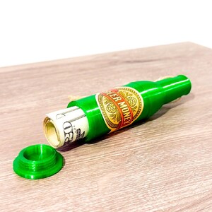Puede incluir: Una botella de pl&aacute;stico verde con forma de botella de cerveza con una etiqueta que dice "Beer Money". La botella est&aacute; abierta y tiene dinero en efectivo enrollado en su interior.