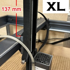 Pu&ograve; includere: Un estrusore per stampante 3D nero con una barra filettata argentata e una manopola nera. L'estrusore &egrave; montato su un telaio in metallo nero. L'estrusore &egrave; etichettato "TOOL" e ha un'etichetta di avvertenza sui laser. L'estrusore &egrave; alto 137 mm.