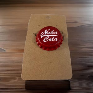 May include: Red bottle cap with white lettering that reads "Nuka Cola".