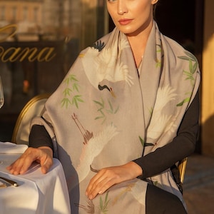 The Crane Bird Pashmina is a semi-sheer, lightweight beige scarf shawl that serves as an elegant wrap