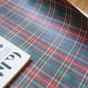 以下が含まれることがあります： 緑、赤、白のチェック柄の包装紙。表紙に「Lab」の文字が入った雑誌が一部見えています。この紙は、ギフトや工芸品に適した、クラシックなタータン模様です。