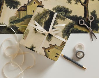 May include: A gift wrapped in beige paper with a vintage illustration of a house and trees. The gift is tied with a white ribbon and bow. There is a spool of white ribbon, a pair of scissors, and two rolls of tape on a white surface.
