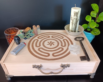May include: A wooden tray with a labyrinth design, featuring a candle with a classical illustration, a small plant, and various ritualistic items. Includes a black skull, a lighter, and a vintage key. The tray has ornate metal handles and feet.