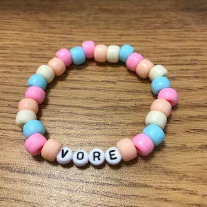 May include: A pastel pink, blue, and yellow beaded bracelet with the word "VORE" spelled out in white beads.