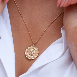 Peut inclure: Un collier en cha&icirc;ne dor&eacute;e avec un grand pendentif circulaire orn&eacute;. Le pendentif pr&eacute;sente un design d&eacute;taill&eacute; et une surface textur&eacute;e.