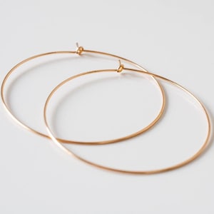 Puede incluir: Un par de pendientes de aro de oro. Los aros son finos y delicados, y están hechos de un metal liso.
