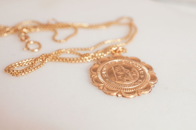 Peut inclure: Un collier en cha&icirc;ne dor&eacute;e avec un grand pendentif rond orn&eacute; d'un motif d&eacute;taill&eacute;. Le pendentif a une surface textur&eacute;e en relief avec une image centrale et une inscription.