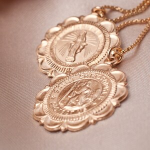 Peut inclure: Deux m&eacute;daillons dor&eacute;s sur un collier &agrave; cha&icirc;ne. Les m&eacute;daillons sont ronds avec des bords festonn&eacute;s et pr&eacute;sentent des images religieuses. Le m&eacute;daillon sup&eacute;rieur repr&eacute;sente une femme avec les mains lev&eacute;es en pri&egrave;re. Le m&eacute;daillon inf&eacute;rieur repr&eacute;sente un homme avec une aur&eacute;ole et une croix. Le texte "SAINT CHRISTOPHER" est visible autour du bord du m&eacute;daillon inf&eacute;rieur.
