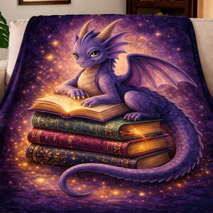 Puede incluir: Una manta de felpa con un dragón púrpura descansando sobre una pila de libros. El dragón tiene ojos verdes y cuernos dorados. Los libros son de varios colores, con detalles dorados. El fondo es un diseño estrellado púrpura y dorado.