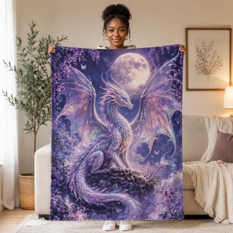 May include: A plush blanket featuring a fantasy dragon illustration. The dragon is white and purple, with large wings, set against a night sky with a full moon. The blanket has a soft, velvety texture.