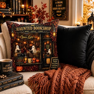 May include: A square throw pillow featuring a printed illustration of a haunted bookshop with ghosts, pumpkins, and autumn leaves. The text reads Haunted Bookshop, Books, Coffee, Curses, Open Late, Enter If You Dare, and Spooky Stories, Stories, Warm Drinks.