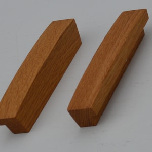 May include: Two wooden cabinet pulls with a curved design. The pulls are made of light brown wood and have a smooth finish.