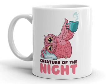 May include: White ceramic mug with a pink owl-like creature holding a teal cup with steam rising. The creature rests on a pillow and the text "CREATURE OF THE NIGHT" is printed below the owl in pink and white.