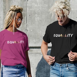 Könnte beinhalten: Zwei Personen tragen T-Shirts mit dem Aufdruck "EQUALITY". Ein Shirt ist magenta, das andere ist schwarz. Das Wort "EQUALITY" ist in Weiß gehalten, wobei die Buchstaben "A" und "L" braun und beige sind.