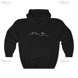 May include: Black hooded sweatshirt with a white minimalist mountain and wave design. The sweatshirt features a front pocket and a drawstring hood. The design is centered on the chest. The brand name "Deckorate Studios" is printed in white on the top left and right corners.
