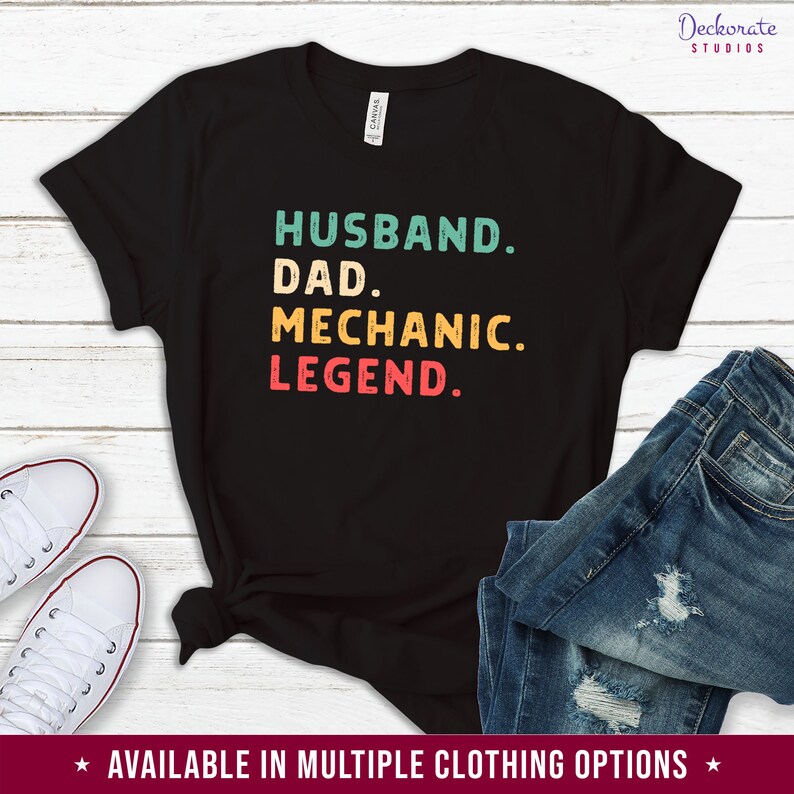 Puede incluir: Camiseta negra con las palabras "HUSBAND. DAD. MECHANIC. LEGEND." en verde azulado, amarillo y rojo. La camiseta se combina con vaqueros azules y zapatillas blancas. El texto "AVAILABLE IN MULTIPLE CLOTHING OPTIONS" est&aacute; en la parte inferior.