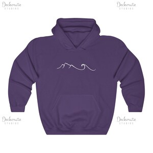 May include: A purple hooded sweatshirt with a front pocket and a white line drawing of mountains and waves. The sweatshirt has a drawstring hood and long sleeves. The design is centered on the chest.