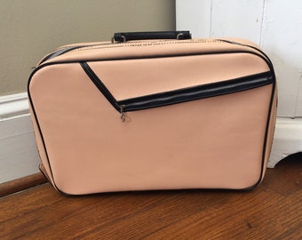 May include: A vintage pink suitcase with a black zipper and trim. The suitcase has a small pocket on the front.