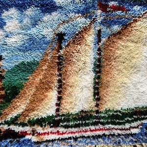 May include: A colorful rug with a sailboat and lighthouse design. The rug is made of a fluffy, textured material and features shades of blue, green, white, red, and brown.