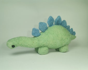 May include: A green and blue felt dinosaur toy with a spiky back. The dinosaur has a small black eye and a long neck.