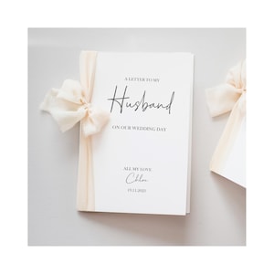 May include: A white wedding card with the text "A Letter to My Husband on Our Wedding Day." The card is tied with a cream-colored ribbon and bow. The name "Chloe" and the date "19.11.2023" are also printed on the card.