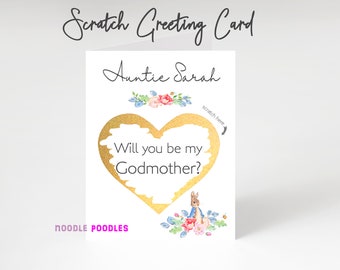Può includere: Un biglietto bianco con un cuore dorato che dice "Vuoi essere la mia madrina?" Il cuore è circondato da fiori e un piccolo coniglio. Il biglietto è indirizzato a "Zia Sarah" e dice "Biglietto di auguri da grattare" in alto.