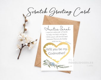 May include: A gold foil scratch-off card with a heart shape and the text "Will you be my Godmother?"  The card has a floral design and the text "Auntie Sarah" with a message asking for help with learning and growing.