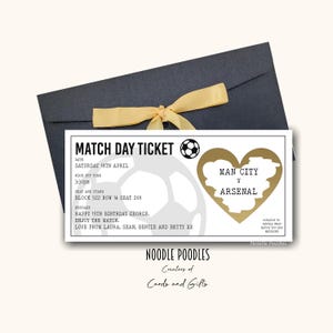 Op de afbeelding: Een voetbalwedstrijdticket voor de wedstrijd Man City tegen Arsenal, gepresenteerd in een donkerblauwe envelop met een gele strik. Het ticket heeft een voetbalafbeelding en de tekst "Match Day Ticket". De datum is zaterdag 18 april.