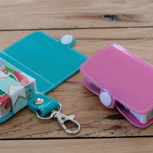 May include: Two small, zippered pouches with keychains. One pouch is teal blue and the other is pink. Both pouches have a clear plastic window and are filled with colorful candies.