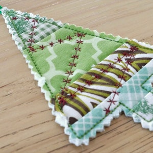 May include: A green, white, and brown patchwork fabric Christmas tree ornament with a scalloped edge.