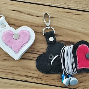 May include: Two heart-shaped leather keychains. One is white with a pink fuzzy heart inside and the other is black with a red heart inside. Both have a silver metal clasp.