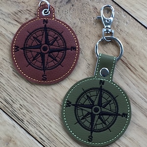 May include: Two leather keychains with compass designs. One is brown with a yellow stitch and the other is green with a white stitch.