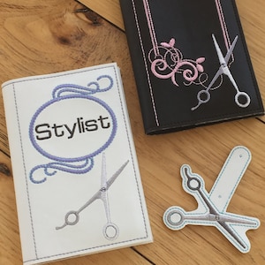 May include: Two white and black fabric covers with embroidered designs. One cover has a circle with the word "Stylist" and a pair of scissors. The other cover has a pink floral design and a pair of scissors. A separate white fabric patch with a pair of scissors is also shown.