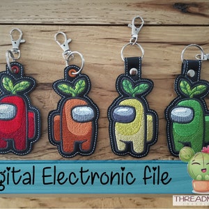 May include: Four embroidered keychains featuring characters from the video game Among Us. The characters are red, orange, yellow, and green. Each character has a small green plant growing on top of their head. The keychains are hanging from silver key rings.