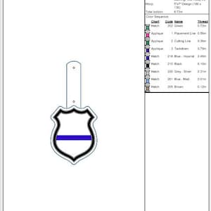 K&ouml;nnte beinhalten: Ein blauer und schwarzer gestickter Patch in Form eines Schildes mit einer d&uuml;nnen blauen Linie in der Mitte. Der Patch ist f&uuml;r eine Druckknopfleiste konzipiert.