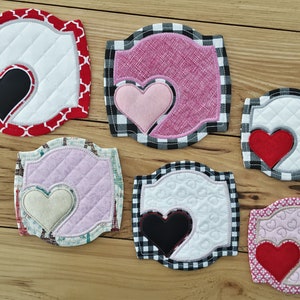 Puede incluir: Seis posavasos de tela acolchada con un diseño de corazón. Los posavasos son de varios colores y patrones, incluyendo rojo, rosa, negro, blanco y gris. Cada posavasos tiene un diseño de corazón diferente, algunos con un corazón sólido y otros con un contorno de corazón.