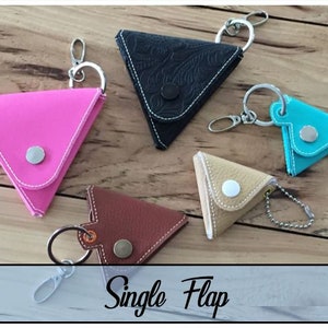 May include: Five triangle-shaped leather coin purses with single flaps and key rings. The purses are in pink, black, beige, brown, and blue.