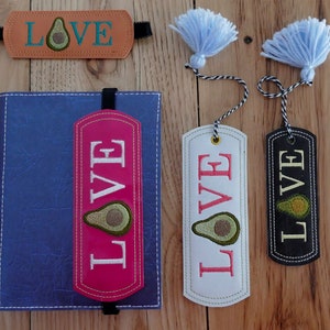 May include: Four handmade bookmarks with the word "LOVE" and an avocado design. The bookmarks are made of leather in different colors: brown, pink, white, and black. Two of the bookmarks have blue tassels.